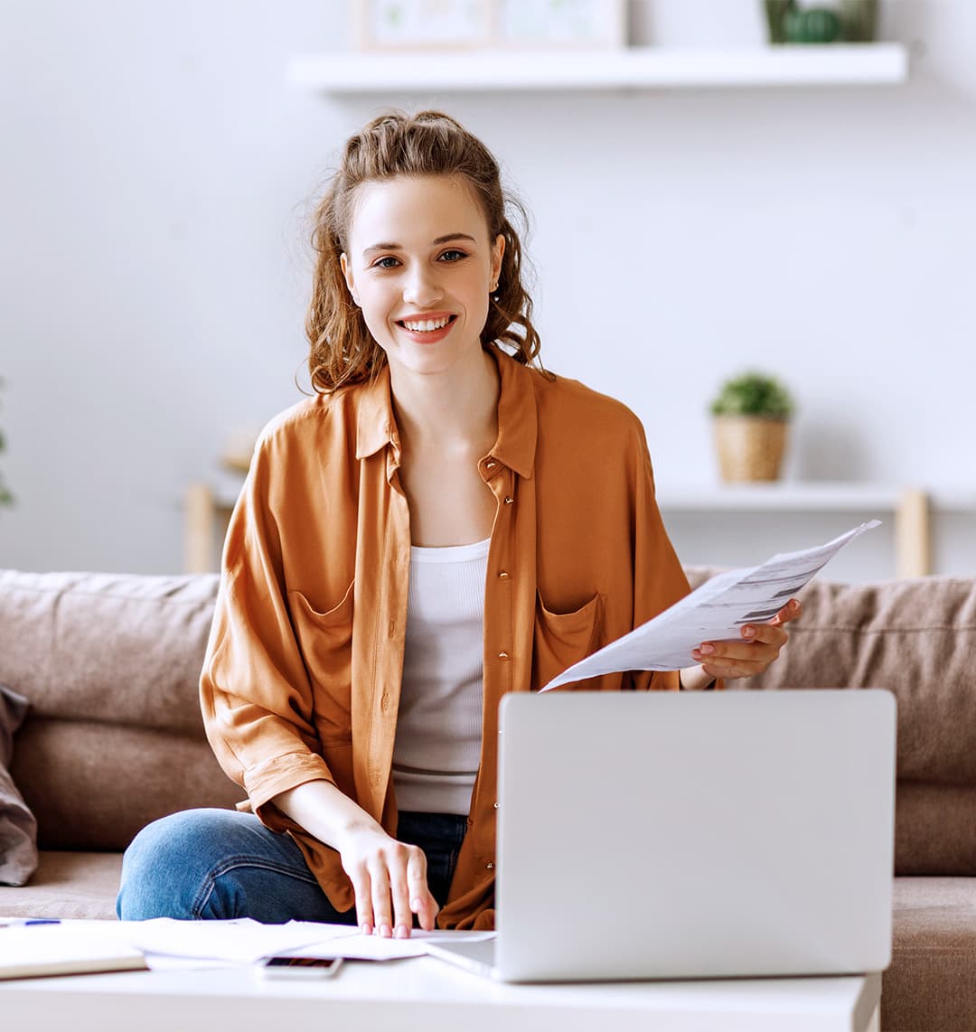 Eine junge Frau sitzt an ihrem Laptop und hält Dokumente in der Hand, während sie sich einen chipTAN-Generator bestellt.