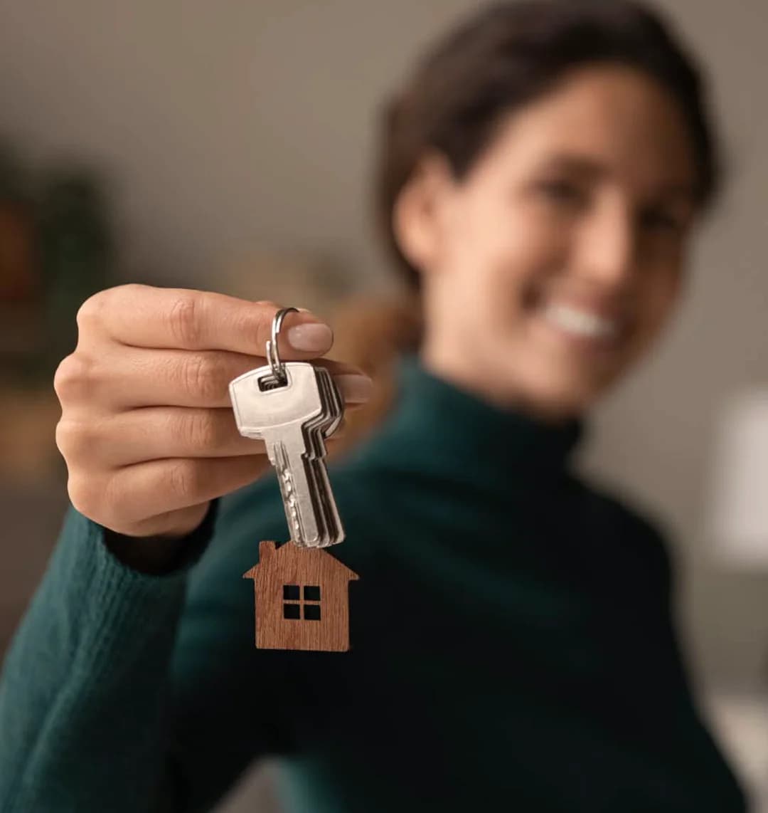 Eine Frau hält einen Schlüssel mit einem Schlüsselanhänger in der Form eines Hauses in der Hand.