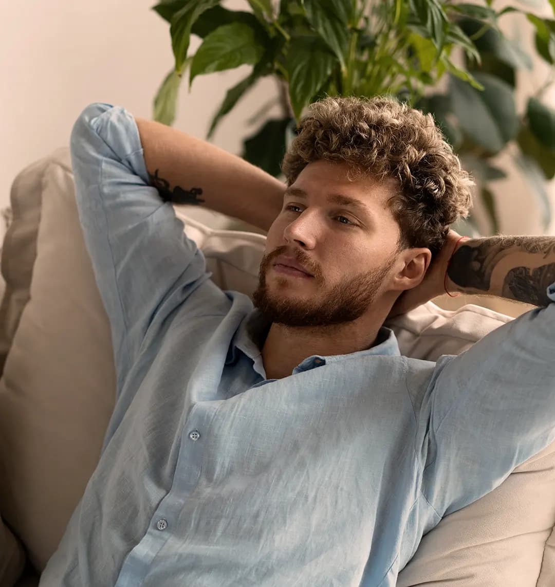 Ein Mann sitzt nachdenklich mit hinter dem Kopf verschränkten Armen auf einem Sofa