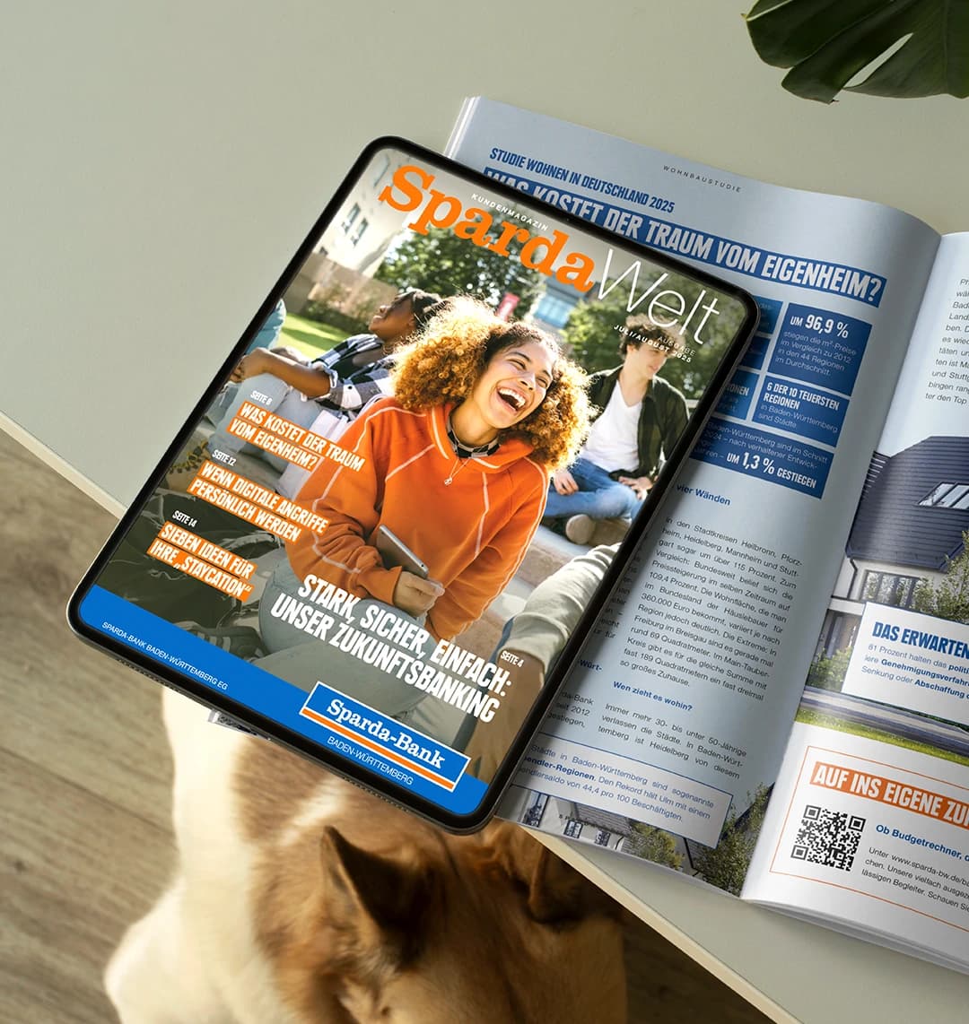 Die Juli/August 2025 Ausgabe des SpardaWelt Kundenmagazins liegt aufgeschlagen auf einem Tisch. Darauf liegt ein IPad, welches das Cover des Magazins zeigt.
