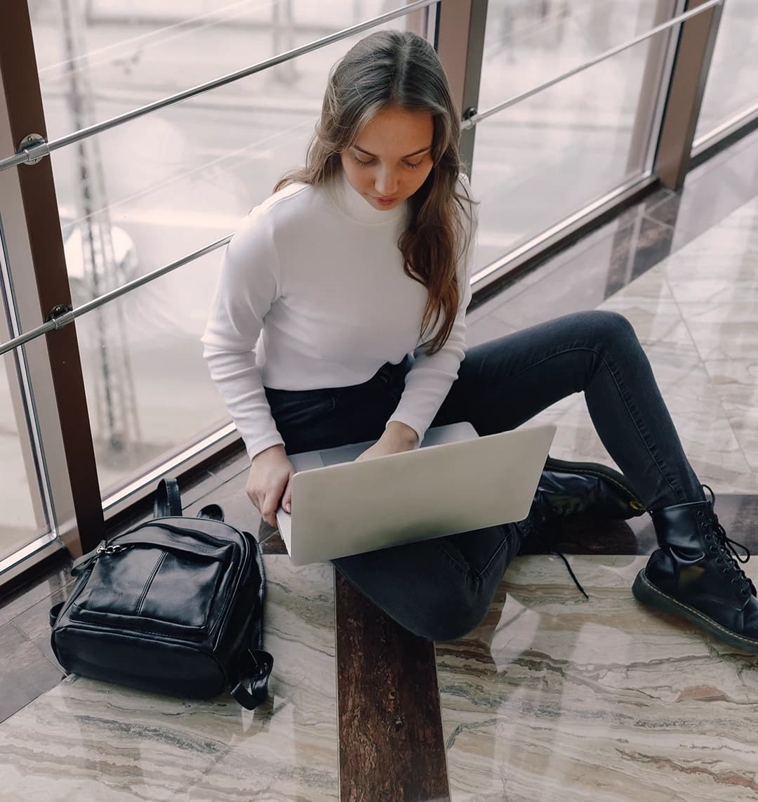 Eine junge Frau sitzt am Flughafen auf dem Boden und arbeitet an ihrem Laptop.