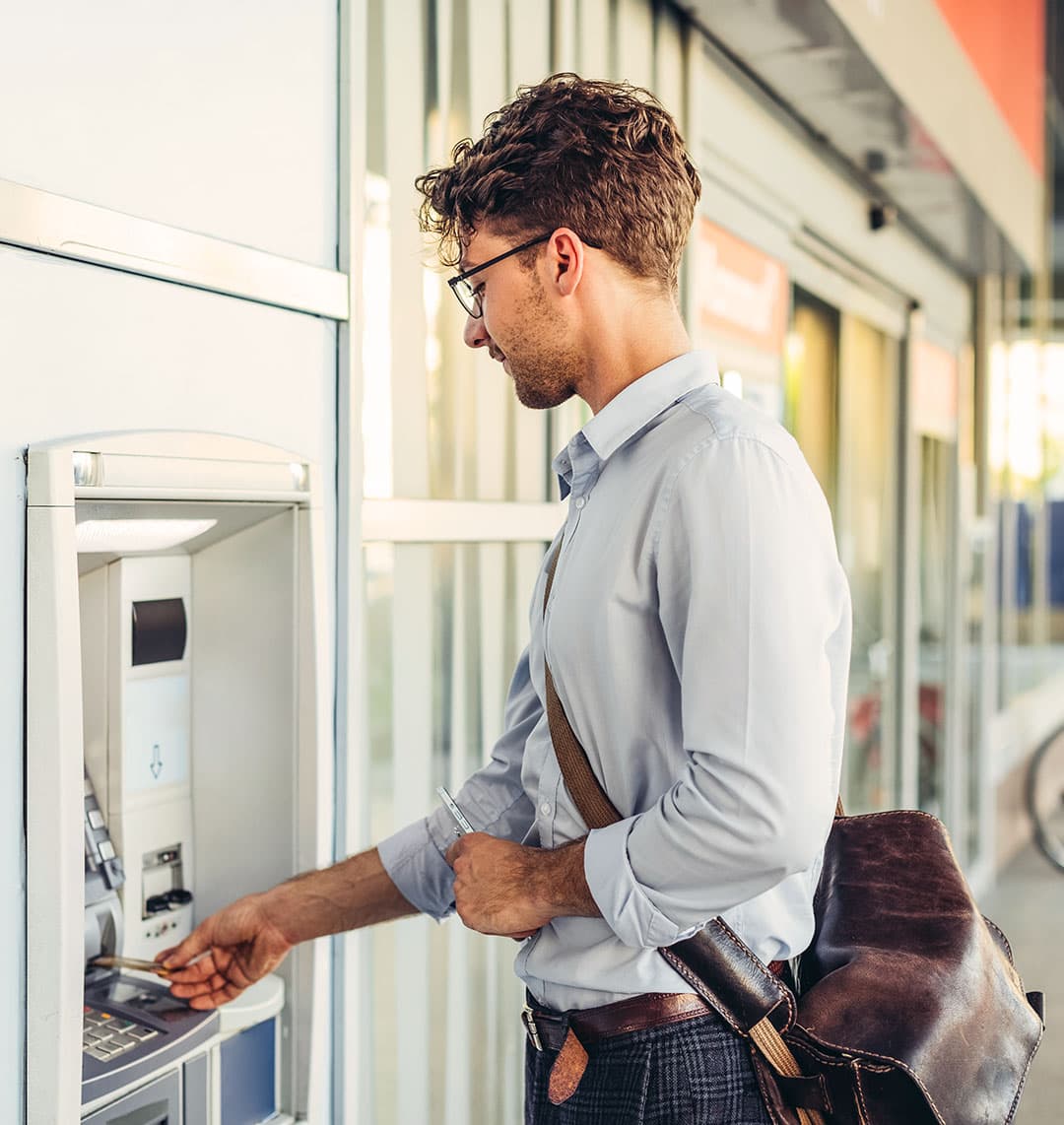 Ein junger Mann steht an einem Bankautomaten, um Geld abzuheben.