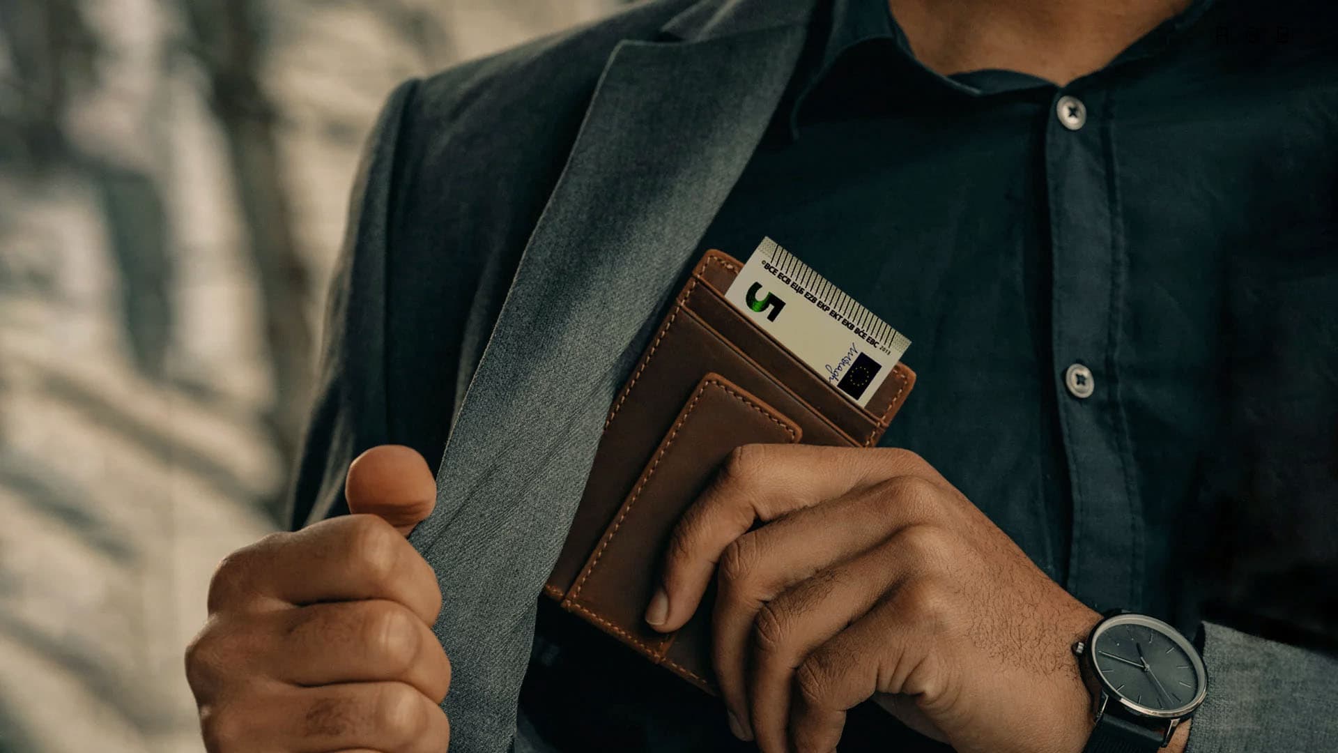 Close-Up von einem Mann der gerade sein Geldbeutel in seine Sakkotasche packt.