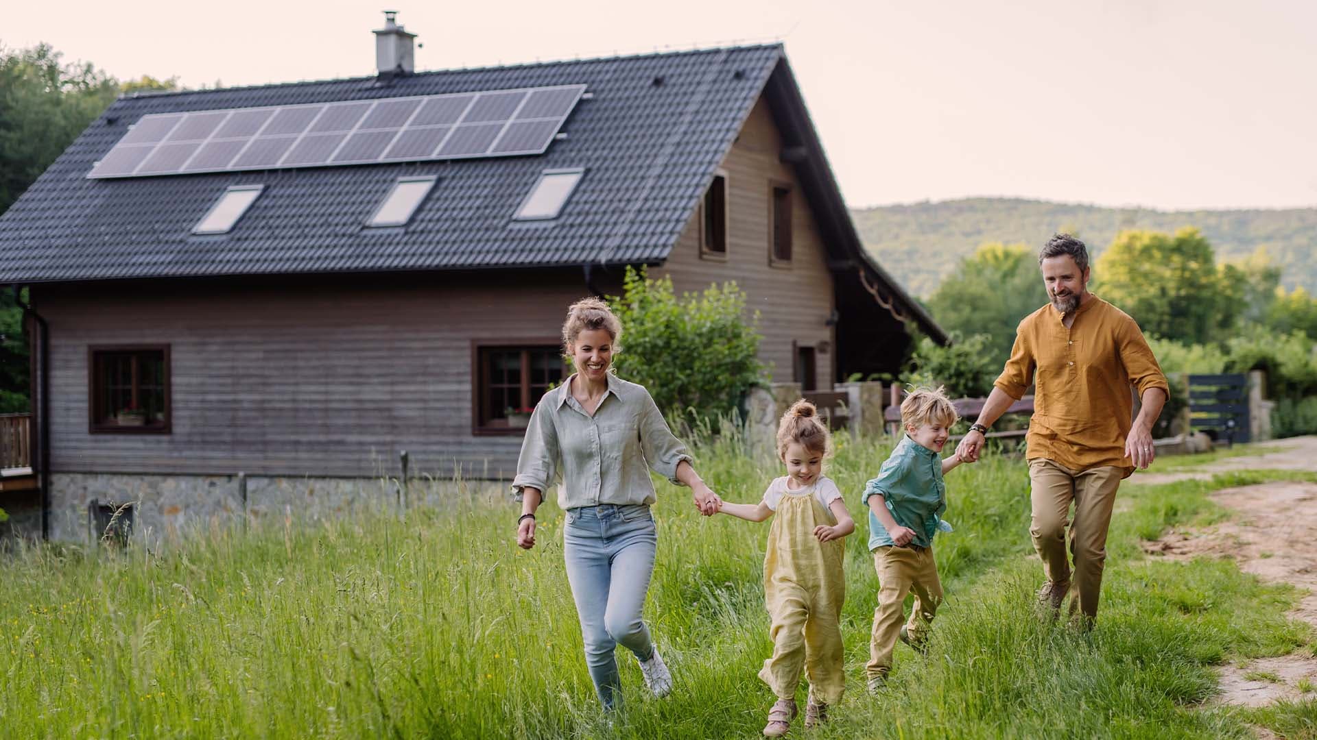 Eine glückliche Familie rennt über eine Wiese. Im Hintergrund steht ihr Haus, dass sie über die Baufinanzierung bei der Sparda BW gekauft haben.