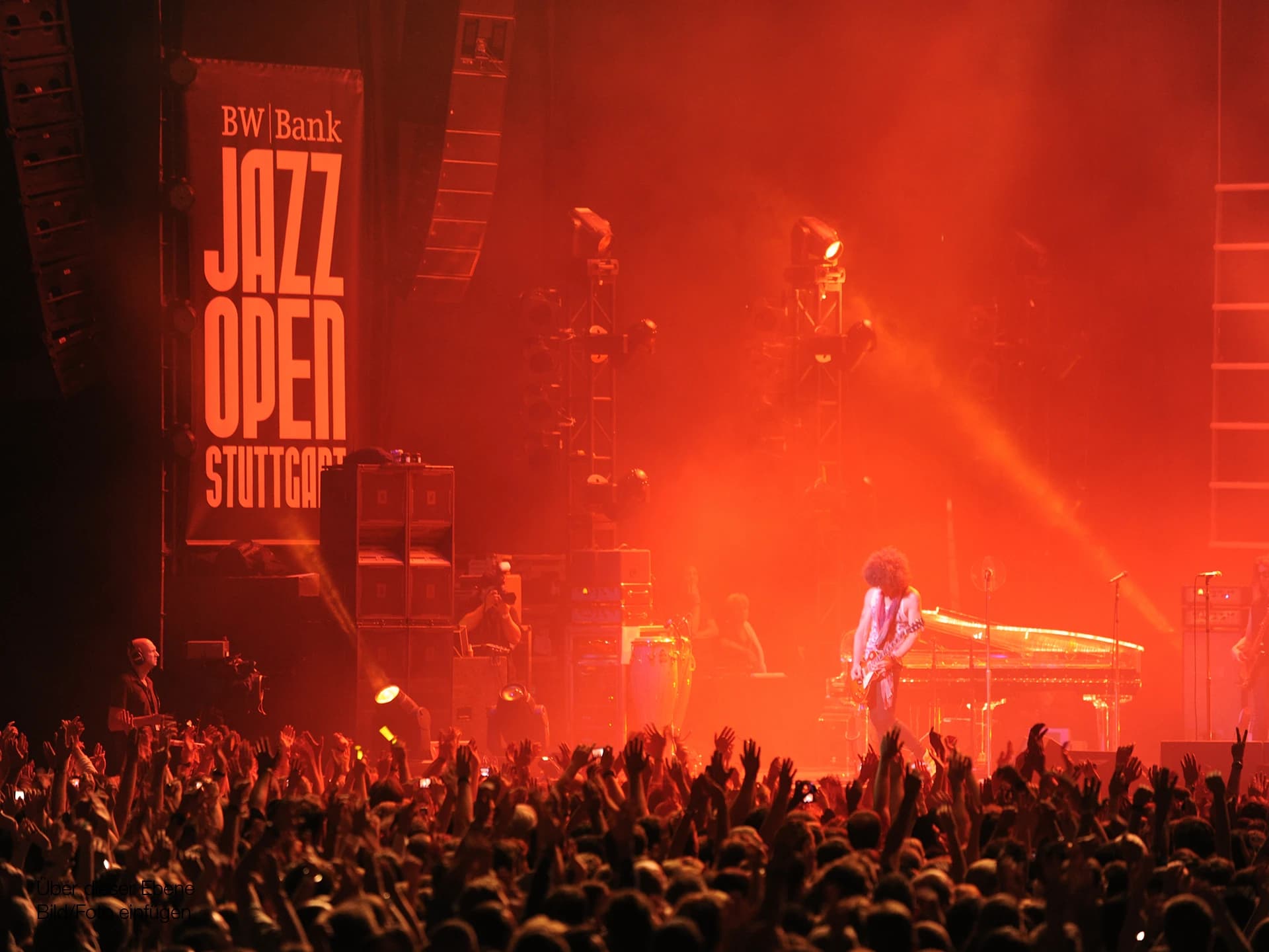 Die Bühne der Jazz Open Stuttgart sind rot erleuchtet. Auf der Bühne steht ein Sänger mit Gitarre.
