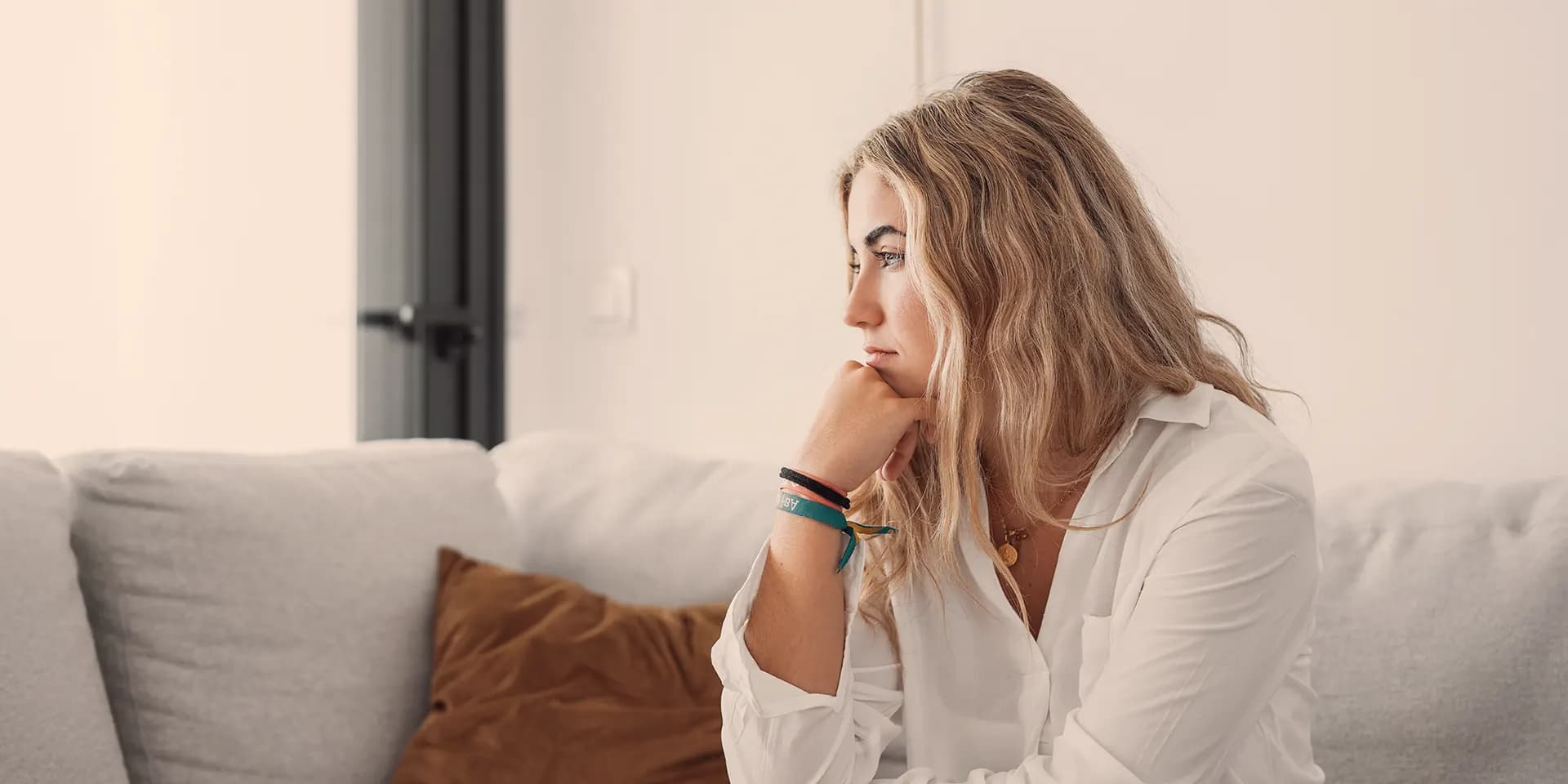 Junge Frau sitzt auf dem Sofa im Wohnzimmer und schaut nachdenklich aus dem Fenster