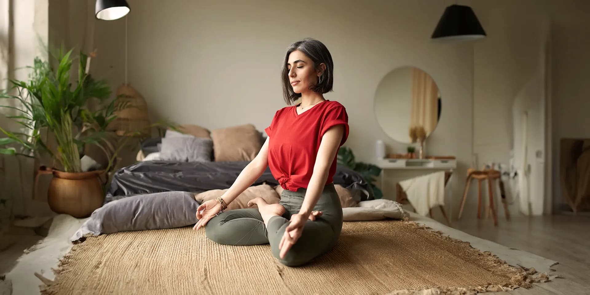 Eine Frau sitzt im Yogasitzt auf dem Fußboden in einem Wohnzimmer