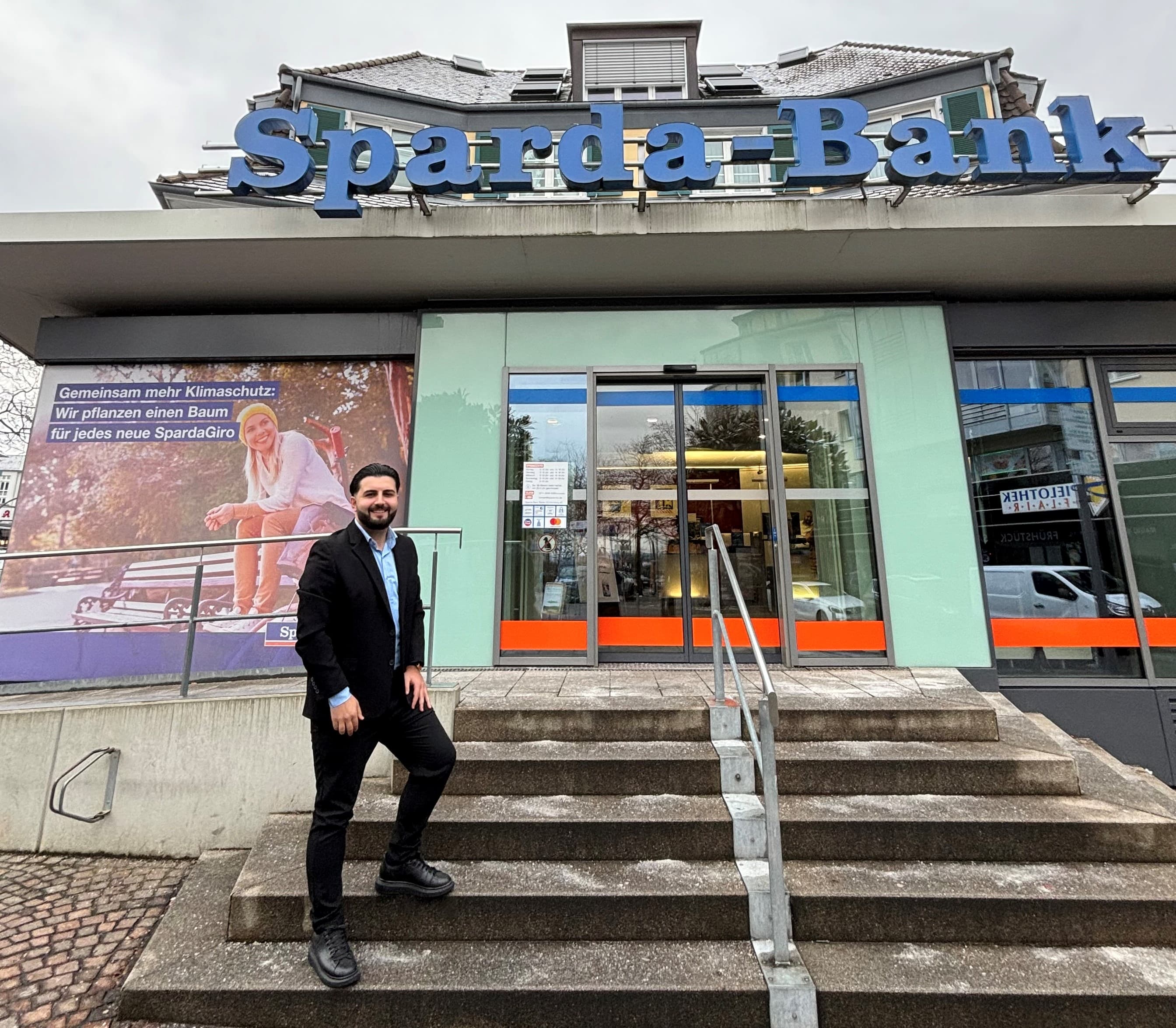 Eine Person im Anzug steht auf einer Treppe, die zu einer Sparda-Bank-Filiale führt.